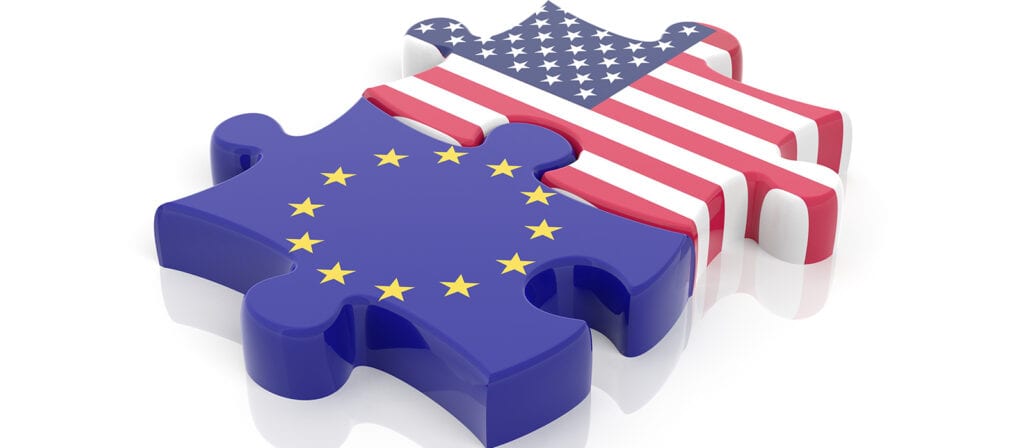 Two interlocking puzzle pieces, one with the flag of the United States and the other with the flag of the European Union, symbolizing a connection or partnership between the US and EU.