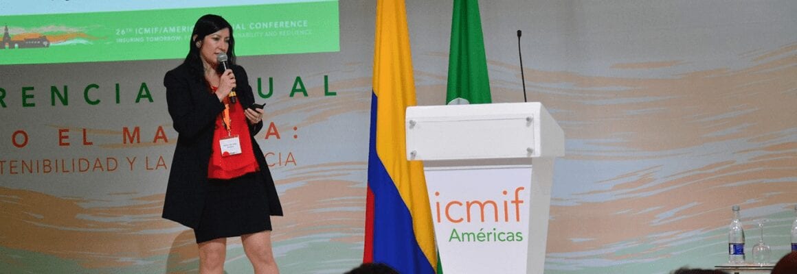 A woman speaks on stage holding a microphone next to a podium with the icmif Américas logo. Behind her are Colombian and green flags, and a conference banner is partially visible in the background.
