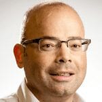 A middle-aged man with glasses, short-cropped hair, and a slight smile, wearing a white collared shirt, against a plain light background.