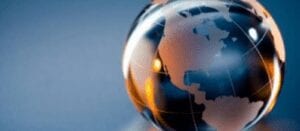 A close-up of a transparent glass globe showing the continents of North and South America, with warm lighting and a blurred blue background.