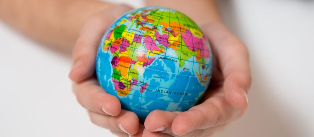 A person gently holds a small, colorful globe in their hands, with visible countries and regions including Africa, Europe, and Asia, symbolizing care and protection for the world.