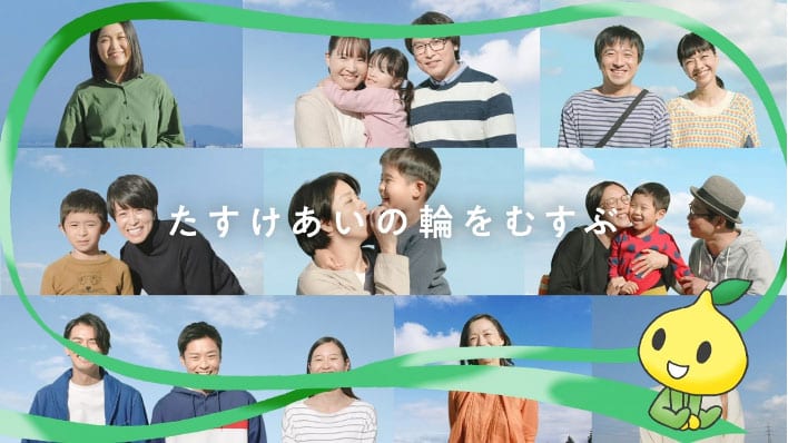 A collage of smiling families and individuals against blue skies, with a green ribbon crossing the image and a cute yellow character in the bottom right. Japanese text is overlaid in white near the center.