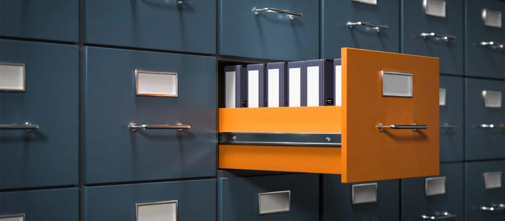 A filing cabinet with multiple blue drawers, one orange drawer pulled open revealing several organized ring binders inside. The other drawers are closed and have blank label holders.
