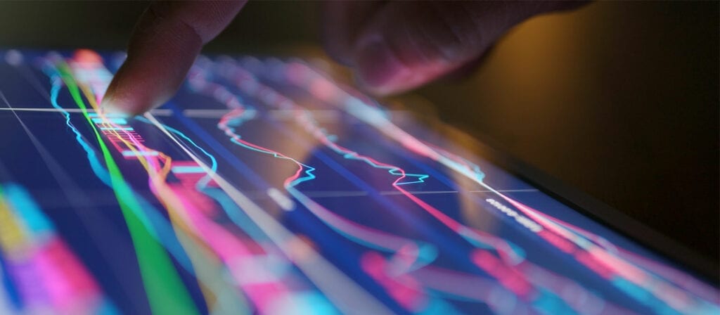 A close-up of a persons finger touching a digital screen displaying colorful financial graphs and charts, indicating data analysis or trading activity.