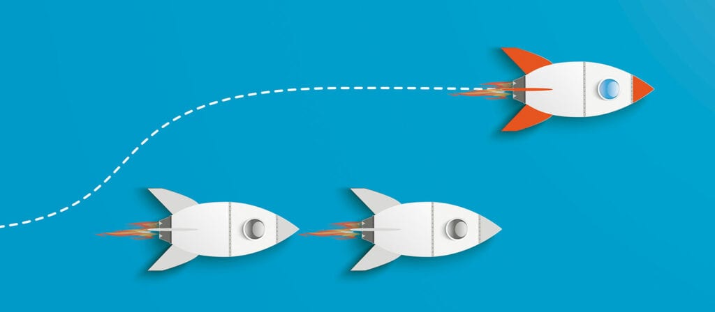 Three rocket ships are flying on a blue background. Two white rockets travel in a straight line, while a third rocket with red fins follows a curved path and leads ahead.