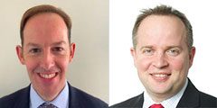 Side-by-side headshots of two men in business attire, both smiling. The man on the left has short brown hair and is wearing a suit and tie. The man on the right has short light hair and is also in a suit and tie.