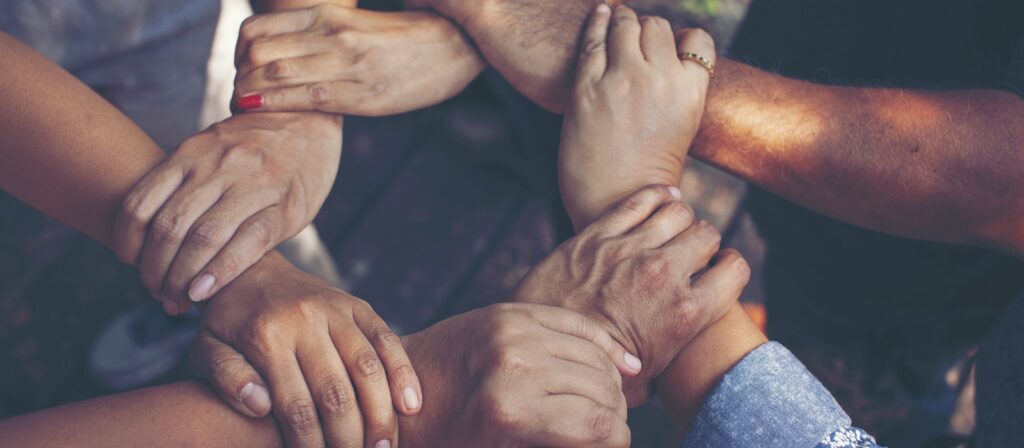 A group of people forming a circle by holding each other’s wrists and hands, symbolizing unity, teamwork, and support.