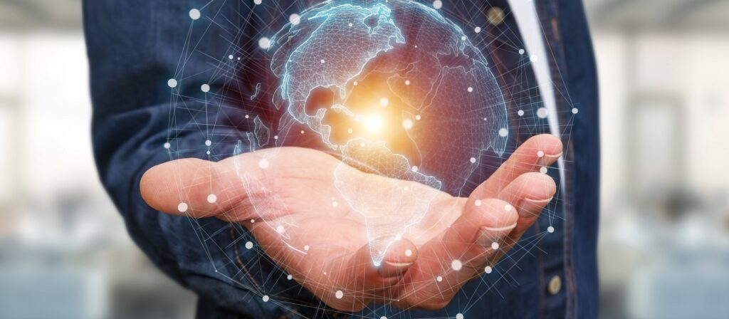 A person holds out their hand with a digital hologram of the Earth hovering above it, surrounded by glowing network lines and dots, symbolizing global connectivity and technology.