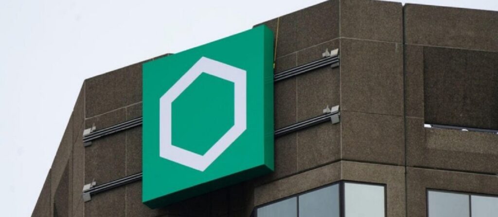 A large green sign with a white hexagon logo is mounted on the upper corner of a concrete office building.