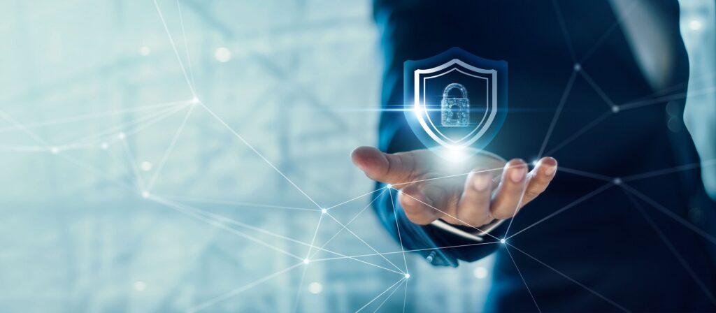 A person in a suit holds out their hand with a glowing digital shield and padlock icon, symbolizing cybersecurity, surrounded by network connections and digital lines.