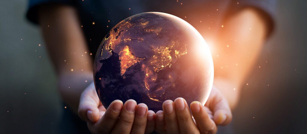 A person holds a glowing Earth in their hands, with illuminated city lights visible on the continents, symbolizing care and responsibility for the planet.