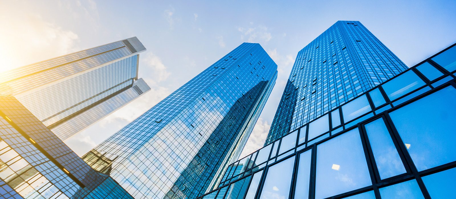 Tall glass skyscrapers reflecting the blue sky and sunlight, viewed from a low angle, with modern architecture and a bright, clear atmosphere.