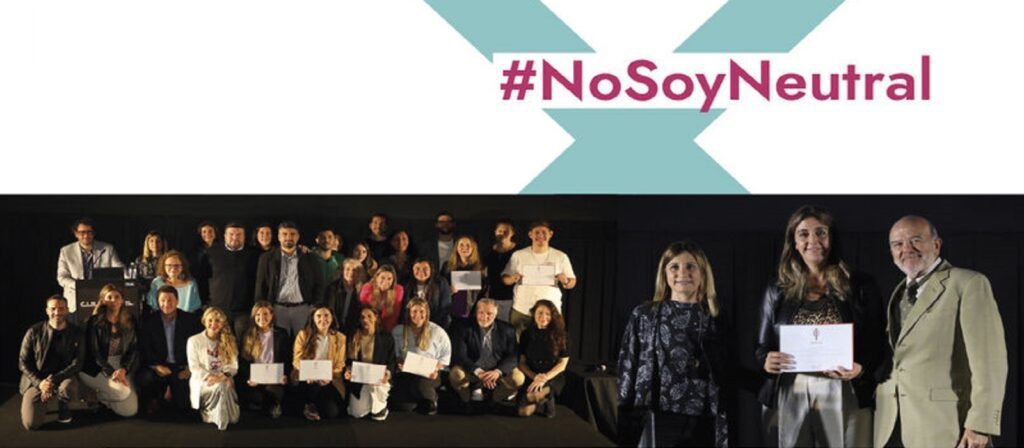 A large group of people pose for a photo on stage, some holding certificates. Above them, the text #NoSoyNeutral is displayed in bold letters.