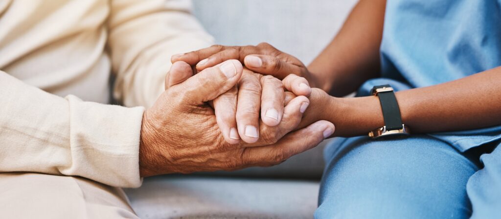 Close-up of a caregiver gently holding the hands of an elderly person, offering comfort and support while sitting together.