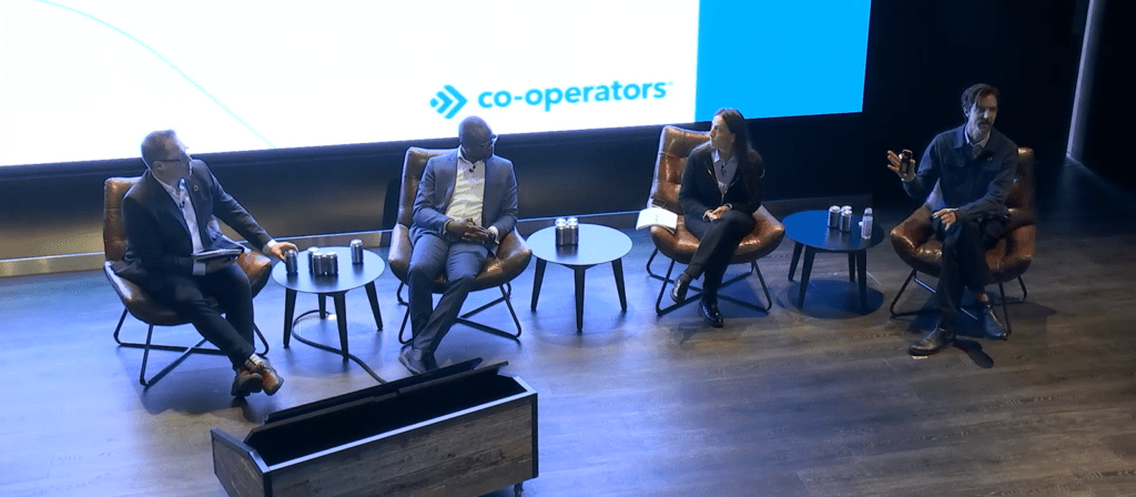 Four people sit on stage in armchairs with small tables between them, having a panel discussion in front of a screen displaying the Co-operators logo.