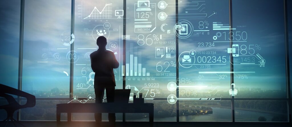 A person stands in front of large windows overlooking a city, with digital data graphics and charts projected in the air, suggesting data analysis or futuristic technology.