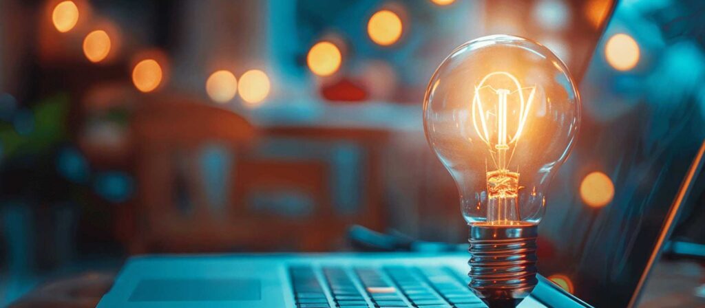 A glowing light bulb sits on top of a laptop keyboard, with blurred warm lights and a cozy indoor atmosphere in the background, symbolizing creativity and ideas in a digital setting.