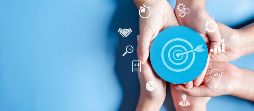 Several hands holding a blue target icon with a dart in the center, surrounded by white business-related icons such as a light bulb, gears, handshake, and magnifying glass on a blue background.