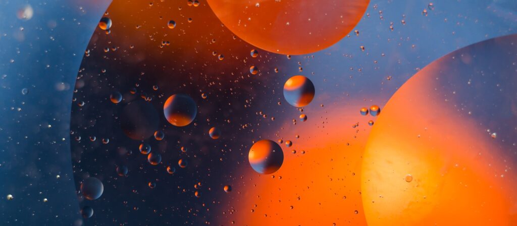 Close-up of abstract liquid bubbles in various sizes, glowing orange and blue against a dark background, creating a cosmic, floating effect.
