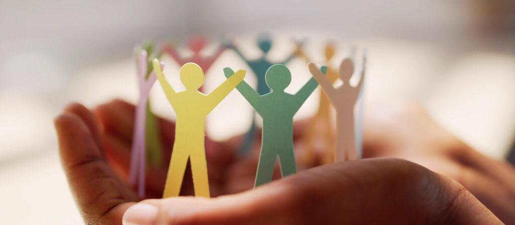 A pair of hands gently holds a circle of colorful paper cutout people, symbolizing unity, community, and support.