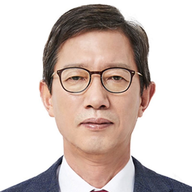 A middle-aged man with short dark hair, wearing round glasses, a navy blue suit, white shirt, and red tie, posing against a plain white background.
