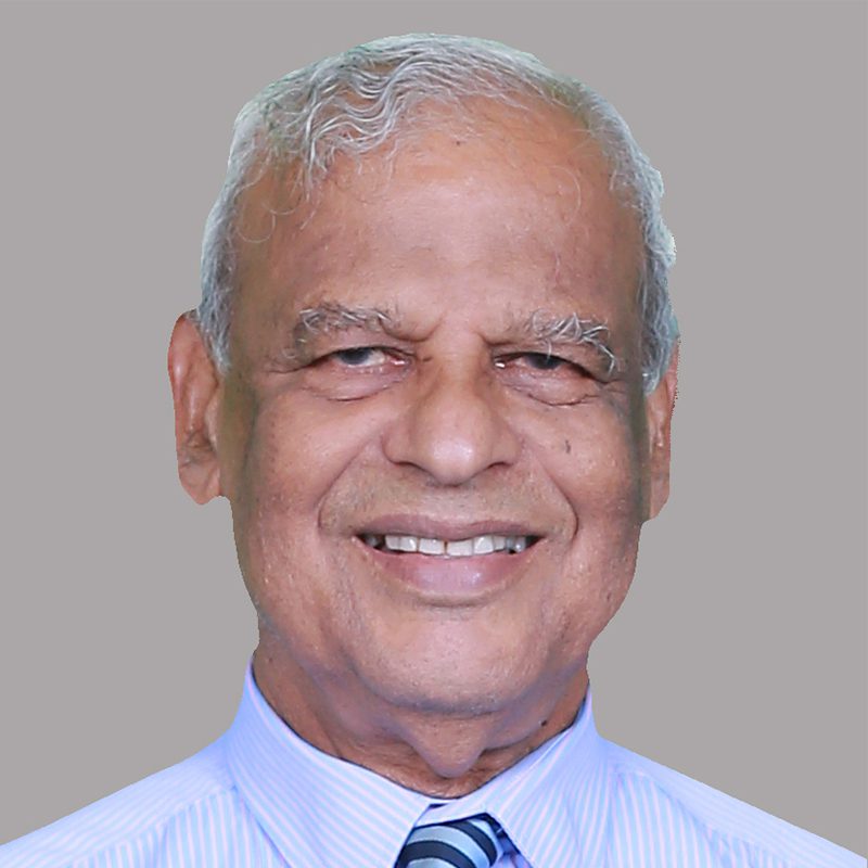 An elderly man with gray hair and a friendly smile, wearing a light blue shirt and striped tie, posed against a plain gray background.