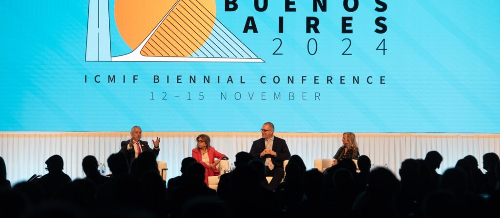 Four people sit on stage in front of a large screen displaying “Buenos Aires 2024 ICMIF Biennial Conference 12–15 November” during a panel discussion at a conference; the audience is visible in silhouette.