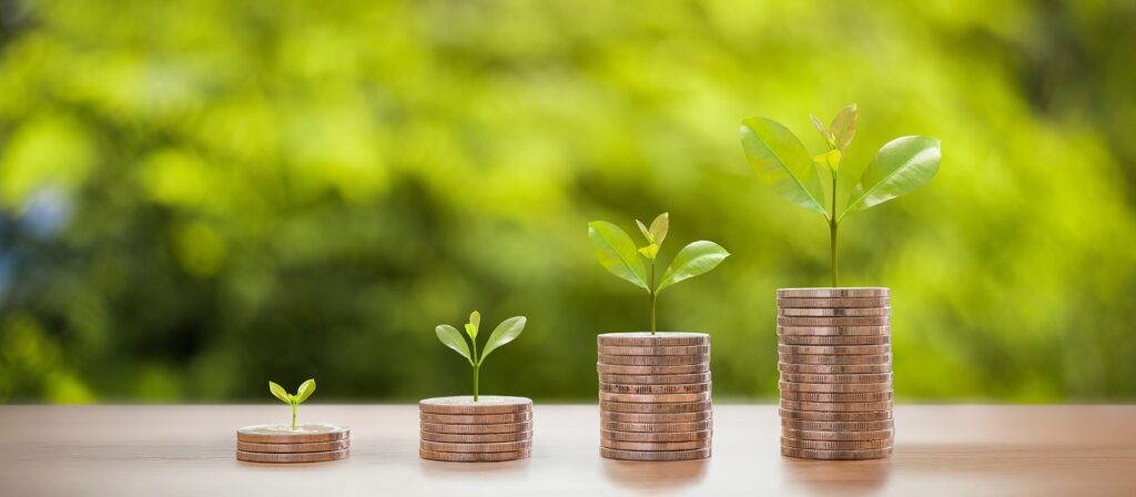 Four stacks of coins arranged in ascending order, each topped with a small growing plant, symbolizing financial growth and investment, with a blurred green natural background.