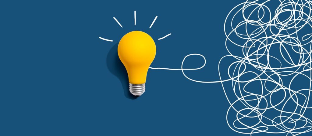 A yellow light bulb on a blue background, with white squiggly lines on the right that become the filament of the bulb, symbolising the concept of ideas emerging from chaos.