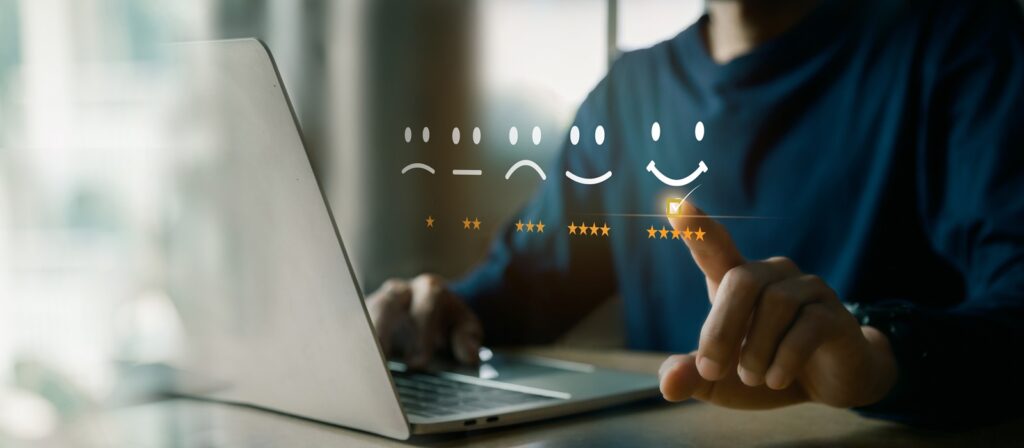 A person using a laptop selects a five-star rating with a smiley face from a digital feedback interface displaying various emotions and star ratings.