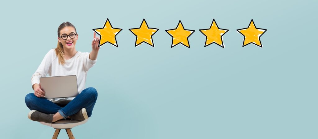 A woman sitting cross-legged on a chair with a laptop on her lap smiles and points at five yellow stars on a light blue background, suggesting a five-star rating or review.