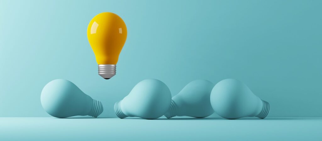 A yellow light bulb floats upright above a row of three blue light bulbs lying on their sides against a blue background, symbolizing creativity and standing out.