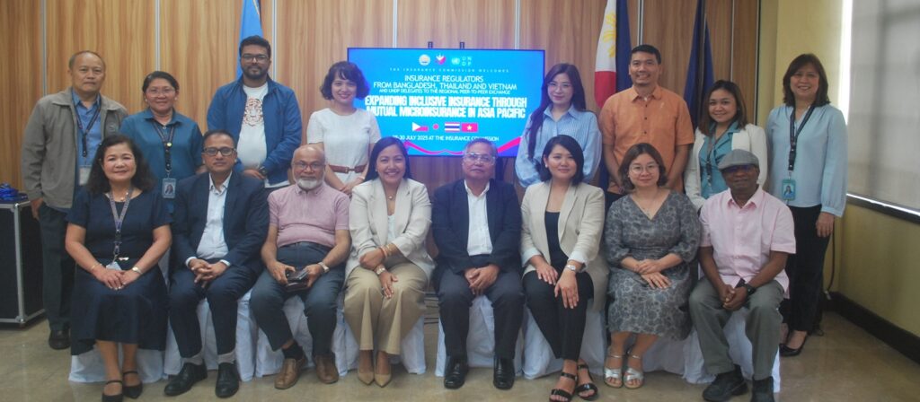 A group of 18 people pose for a photo indoors in front of a screen displaying the title of an education-related event. Most are standing, while six are seated in front. Flags and curtains are visible in the background.