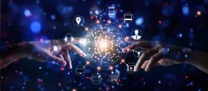 Two hands reach towards a glowing, networked digital sphere surrounded by technology icons such as email, shopping trolley, trophy, and globe, symbolising digital connectivity and communication, with a blue, abstract background.