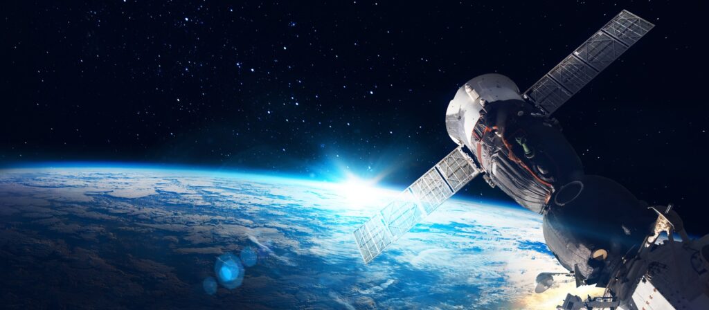 A satellite or spacecraft orbits above Earth, with the sun rising over the planet’s curved horizon and space filled with stars in the background.