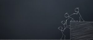 Chalk drawing of four stick figures helping each other climb over a ledge, symbolising teamwork and support, on a dark chalkboard background.