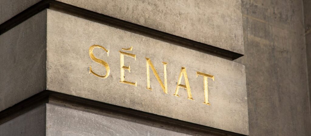 The word Sénat is engraved in gold letters on a stone wall, indicating the French Senate building.