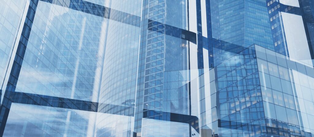 A modern cityscape with tall glass skyscrapers reflecting the sky and surrounding buildings, creating abstract geometric patterns with blue and white tones.