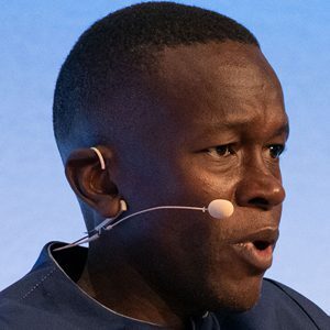 A man speaking into a headset microphone, photographed in profile against a blue background.